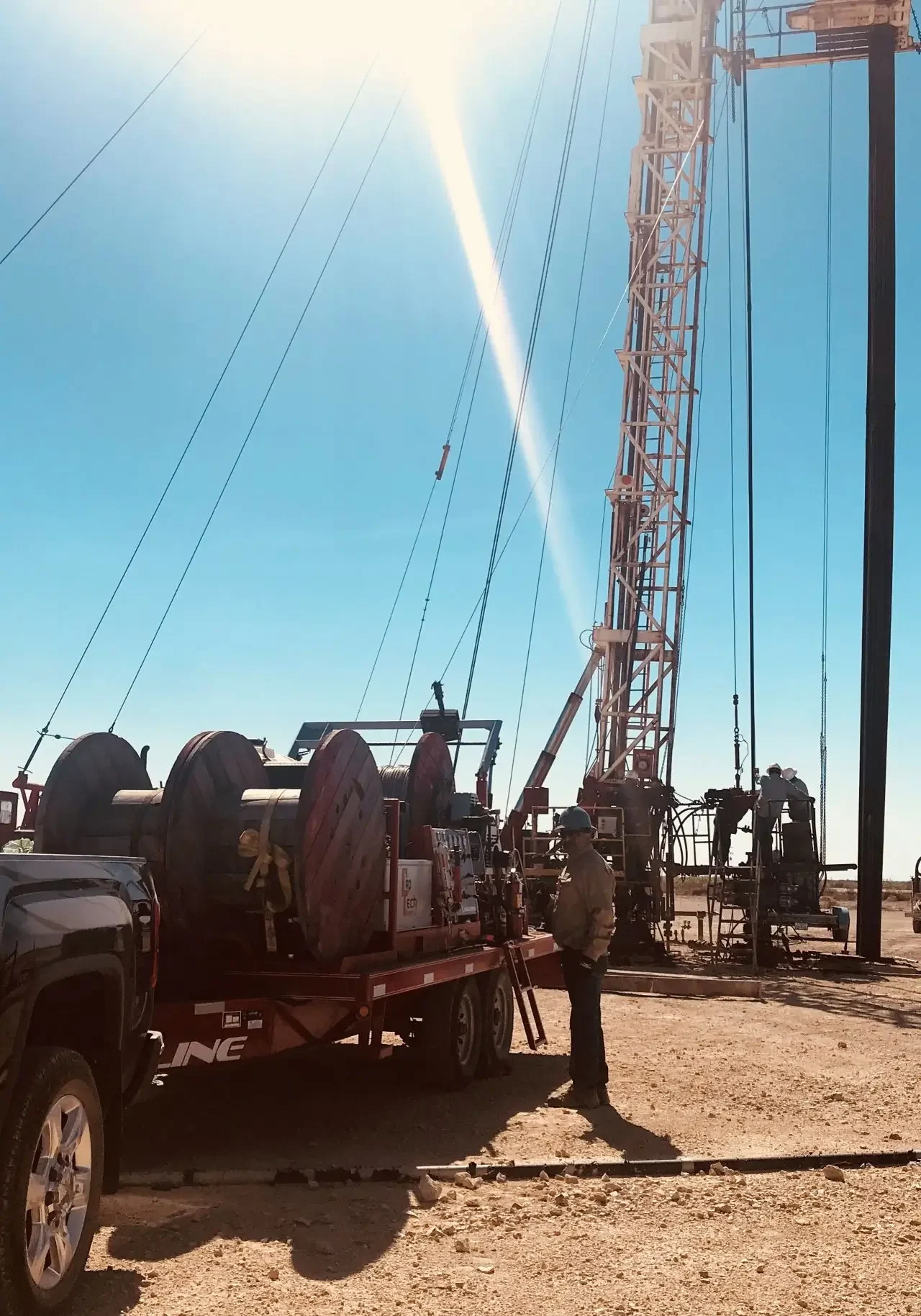 Drilling rig set up in a sunny, open field with a truck nearby.