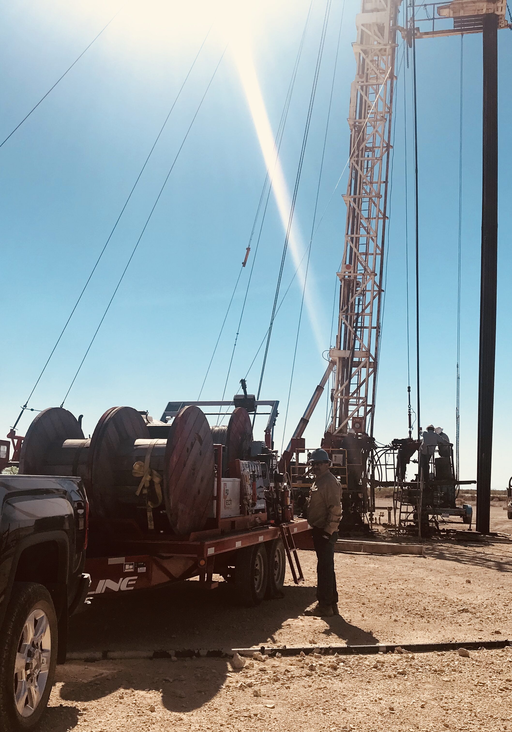 Drilling rig set up in a sunny, open field with a truck nearby.