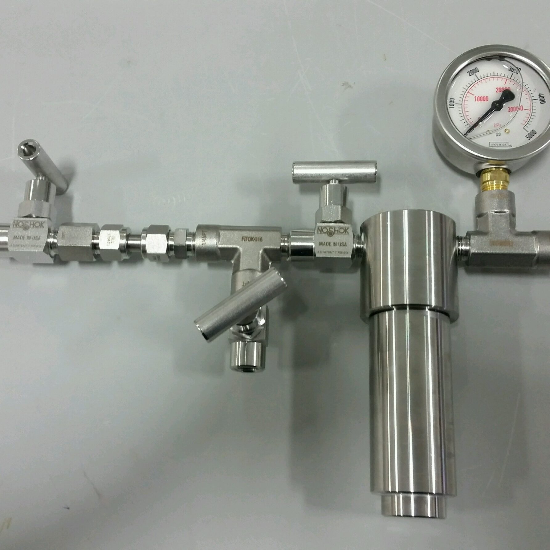 A stainless steel pressure regulator with gauge and fittings on a gray surface.
