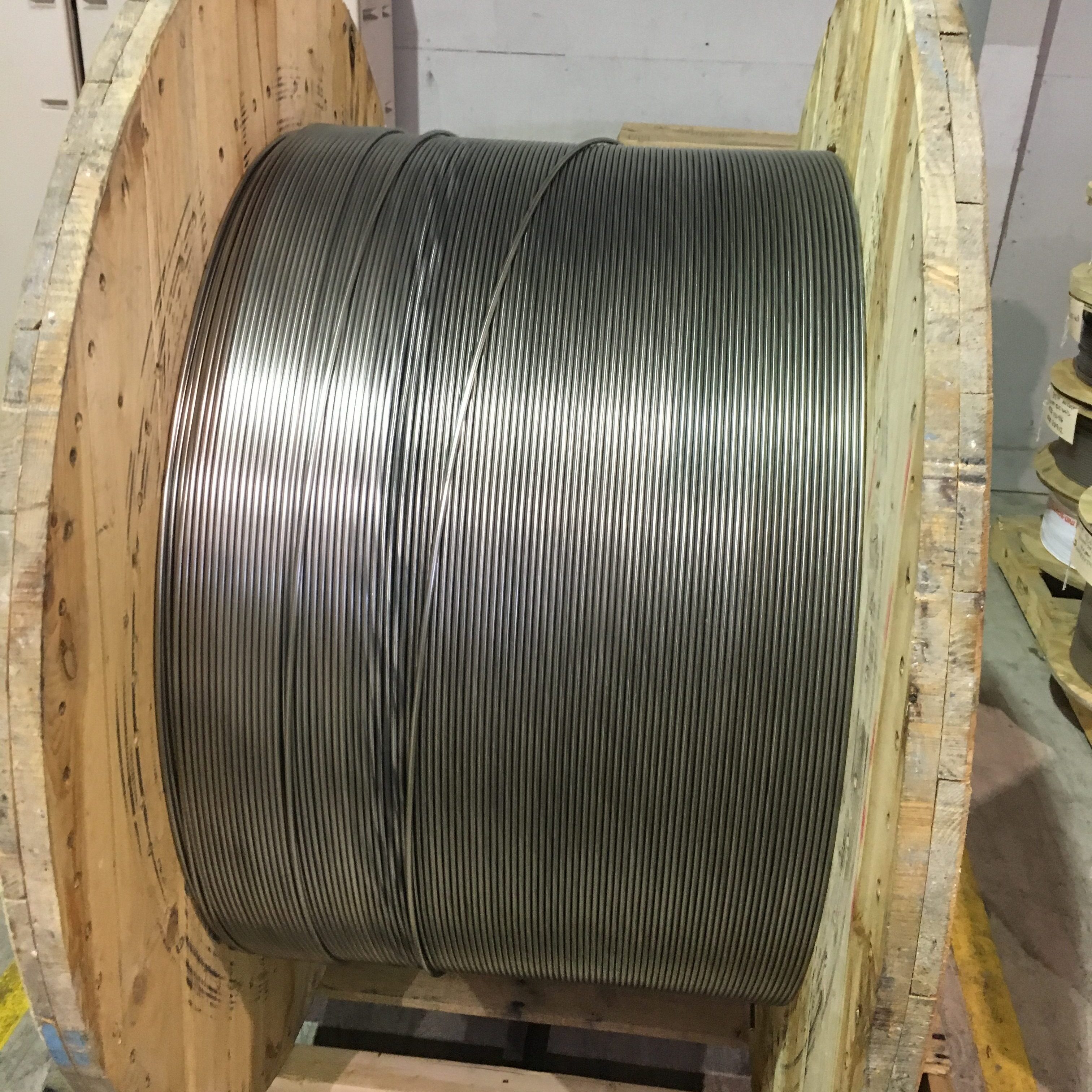 Large spool of steel cable wound on wooden reel in industrial setting.